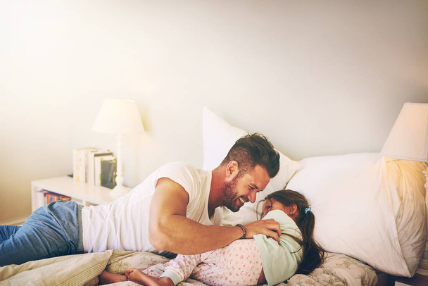 At home with dad. Shot of a cheerful father and daughter having a tickle fight on the bed at home. - Фото, изображение