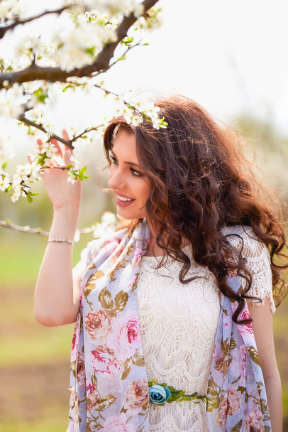 Portrait of a beautiful woman with long hair near flowering trees in spring. - Foto, Imagen