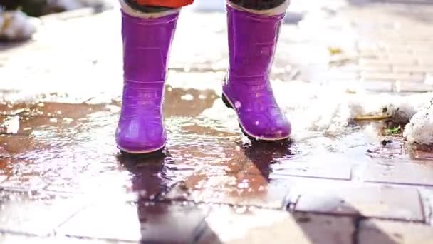 Child jumps on puddles in rubber boots at sunset lights in spring time - 映像、動画
