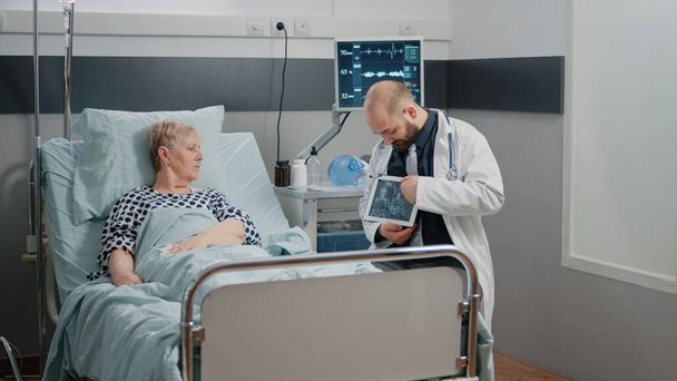 Medic wijzend op tablet display met radiografie voor zieke vrouw - Foto, afbeelding