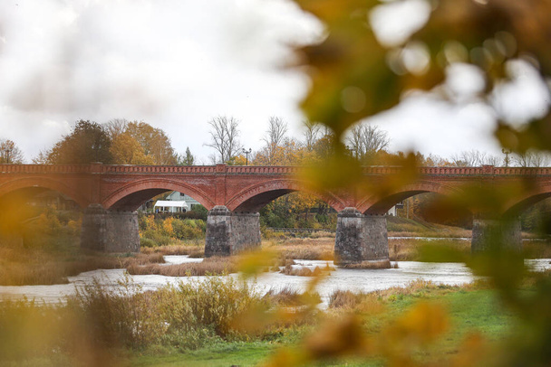 Autumn weather view of old red brick over Venta river in small countryside city Kuldiga, Latvia. Photo taken on a warm overcast autumn day. - Photo, Image