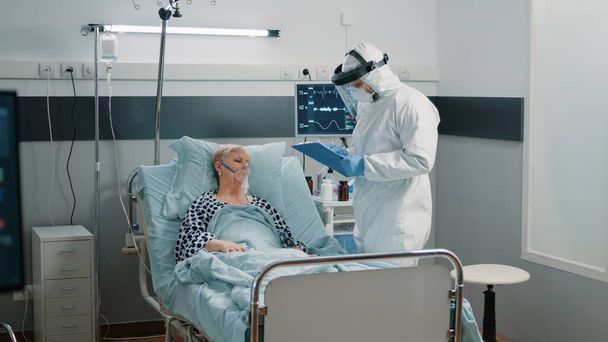 Médico con control de traje protector en monitor de frecuencia cardíaca - Foto, Imagen