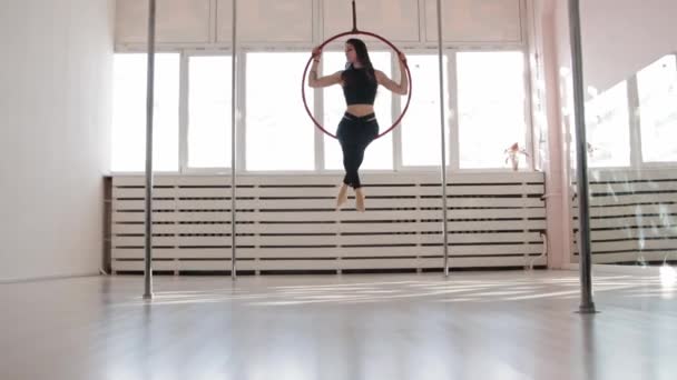 Een jonge vrouw zit de gymnastieke ring en draait rond in de witte studio - Video