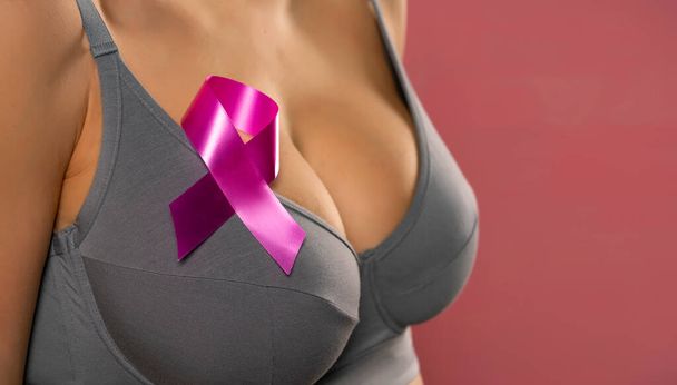 Close up jovem mulher em sutiã cinza com fita de consciência de câncer no fundo rosa - Foto, Imagem