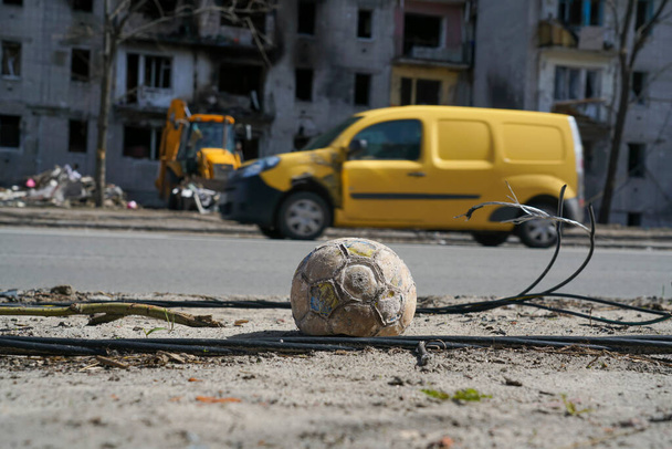 A children's soccer ball lies near the road against a building destroyed by an explosion in the war in Ukraine. Nearby are the wires of a broken power line. - Фото, изображение