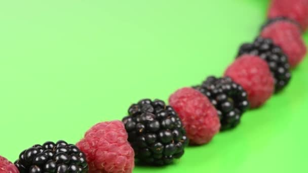 Raspberries alternate with blackberries on green background. Movement from the lower left corner to the upper right corner. Side view. Loop motion. Rotation 360. 4K UHD video footage 3840X2160. - Кадры, видео
