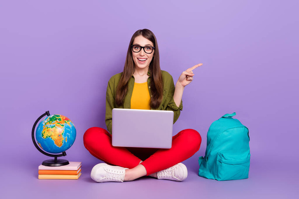 Portrait of attractive cheery girl using laptop showing copy space ad doing homework isolated over violet purple color background - Foto, Bild