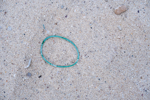 Las bandas de goma verdes fueron dejadas en la playa de arena, por lo que es basura. - Foto, Imagen