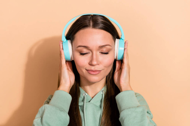 Portrait of attractive serene brown-haired girl listening hit single stereo isolated over beige pastel color background - Foto, Bild