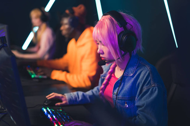 Modern internet tournament. Young pink-haired girl in headset using desktop computer, and colorful keyboard, trying to win her first match. - Foto, afbeelding