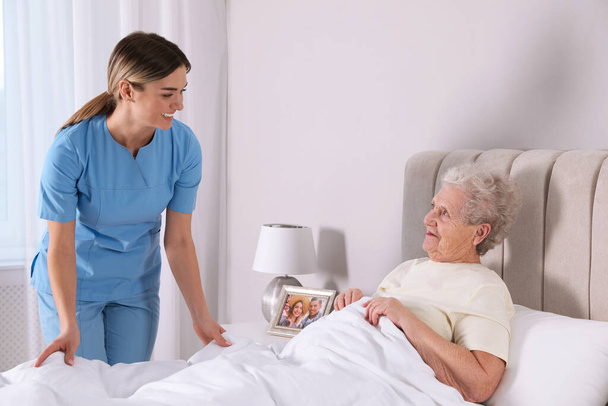 Young caregiver assisting senior woman in bedroom. Home health care service - Фото, изображение