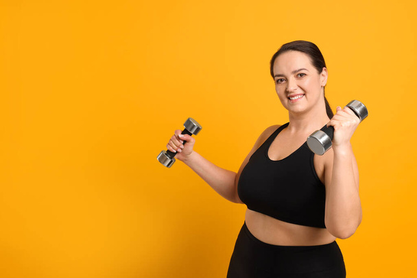 Happy overweight woman doing exercise with dumbbells on orange background, space for text - Foto, immagini