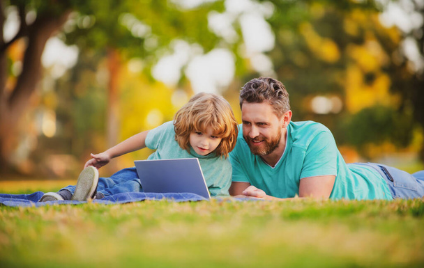 Son with father watching lesson on laptop outdoors. - Фото, изображение
