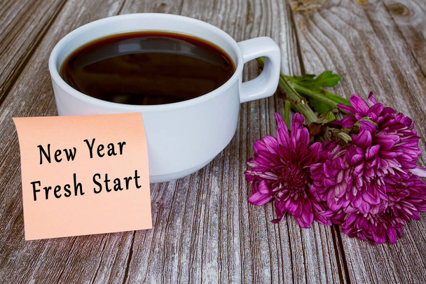 Texte écrit sur une note collante avec tasse à café blanche et fleurs - Nouvel an nouveau départ. Nouvelle année concept. - Photo, image