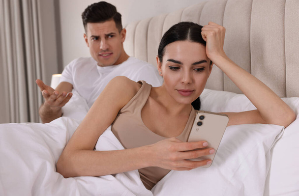 Internet addiction. Woman with smartphone ignoring her boyfriend in bedroom - Fotó, kép