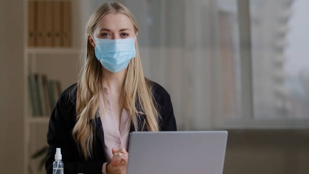 Funny humorous business woman worker in office sitting at table feels cold suffering from flu virus puts on three protective medical face masks fear of contracting coronavirus pandemic safety rules - Фото, зображення