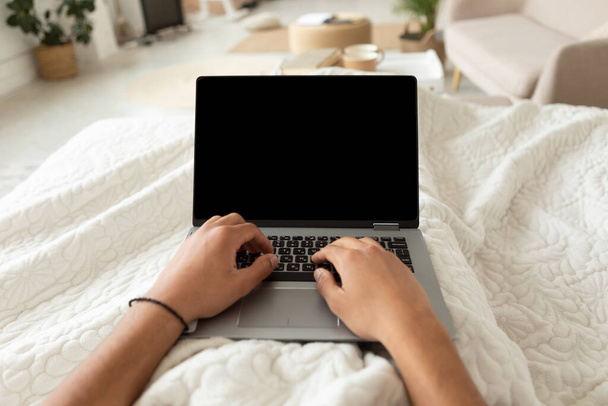 Przycięte ujęcie człowieka za pomocą laptopa pracy leżącej w sypialni - Zdjęcie, obraz