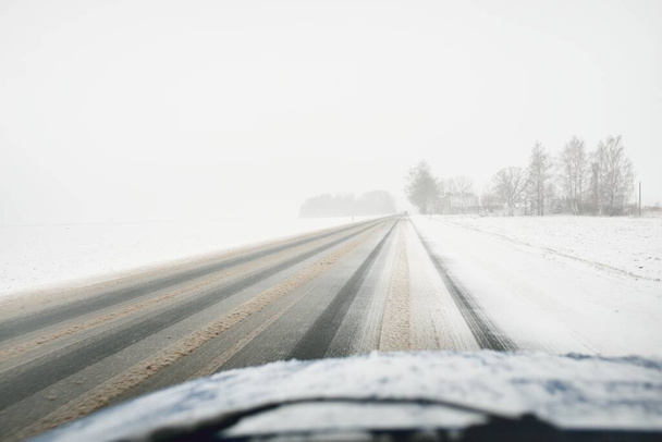 Leere Autobahn (Asphaltstraße) durch schneebedeckten Wald und Felder, ländliche Gegend. Blizzard, Schneeverwehungen. Europa. Natur, Weihnachtsurlaub, abgelegene Orte, Winterreifen, gefährliches Fahrkonzept - Foto, Bild