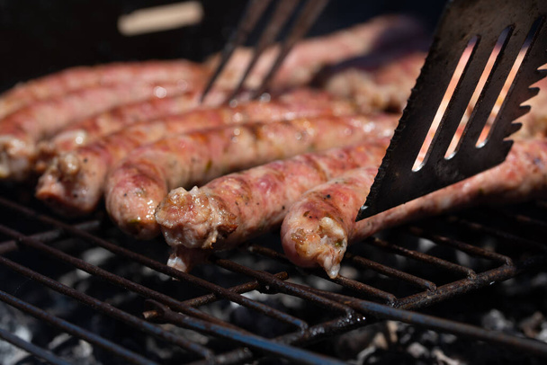 Sausages, traditional Italian 'salsiccia', being turned by a metal shovel, grill on a rustic grill over hot charcoal - Photo, Image