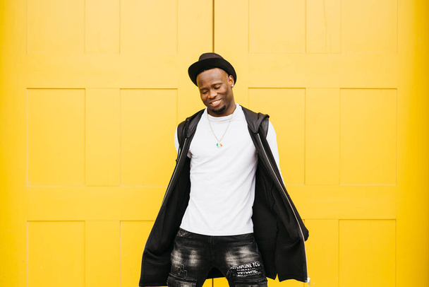 Portrait of a young smiling black male standing against a yellow door - Фото, изображение