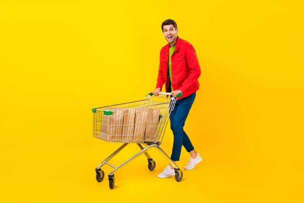 Full size photo of impressed young brunet guy do shopping wear jacket pants shoes isolated on yellow background - Фото, изображение