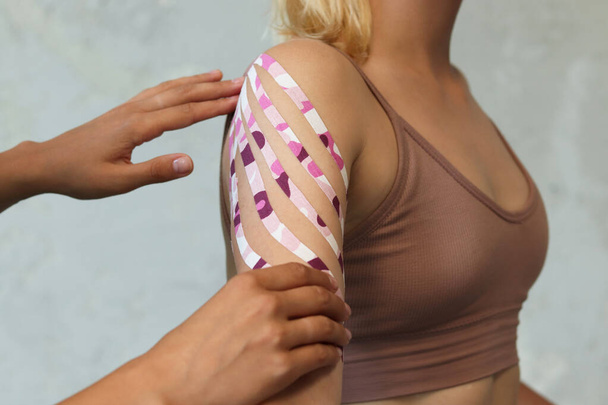 Donna con del nastro adesivo sul braccio e sulla spalla. Fissaggio dei muscoli del bicipite con un cerotto per la kinesio terapia. - Foto, immagini