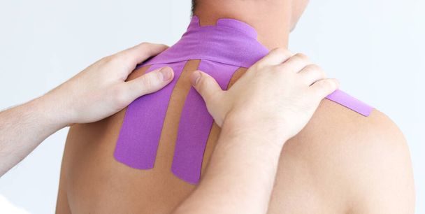 Kinesiology taping. Kinesiology tape on patient neck. Young male athlete on white background. Post traumatic rehabilitation,sport physical therapy, recovery concept, alternative medicine. - Фото, изображение