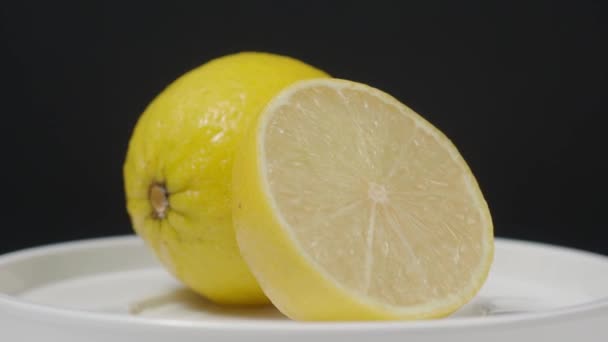 Délicieux citron se déplaçant sur la platine. Savoureux citrons isoler sur le fond noir. Des citrons entiers et demi-jaunes sont isolés sur fond sombre. de près. Représenter un menu de boissons acides et rafraîchissantes. - Séquence, vidéo