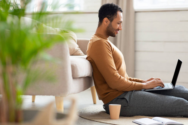 Arab férfi használ laptop ül a padlón otthon - Fotó, kép