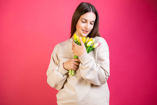 Happy young woman enjoy bouquet of tulips on pink background. - 写真・画像