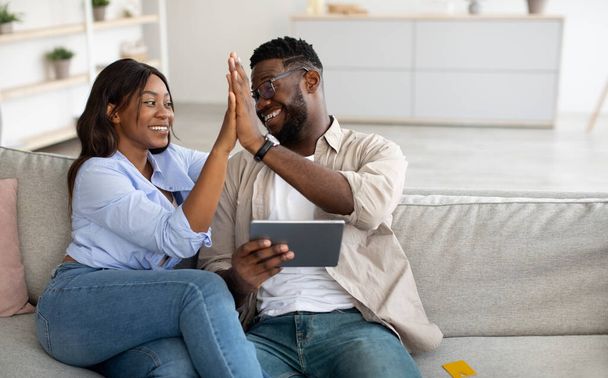 Feliz pareja negra usando la tableta, celebrando la victoria dando cinco altos - Foto, imagen