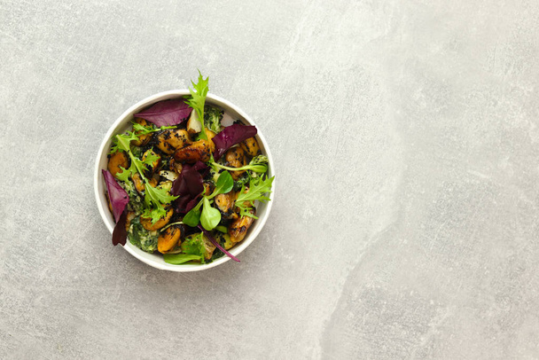 Salad with mussels, arugula and greens in a round takeaway paper container on gray background. Healthy food delivery concept. Banner. Top view. Free space for text. - Foto, imagen