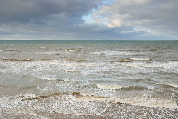 Blick auf die Ostsee von einem sandigen Ufer (Sanddünen). Klarer Himmel mit glühenden Wolken, Wellen und Wasserspritzern. Idyllische Meereslandschaft. Warmes Winterwetter, Klimawandel, Natur - Foto, Bild