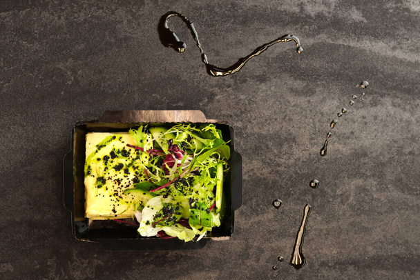 omeleta francesa e verdes e salada de pepino em um recipiente de papel em um fundo cinza. Pequeno-almoço. Conceito de entrega de alimentos saudáveis. - Foto, Imagem