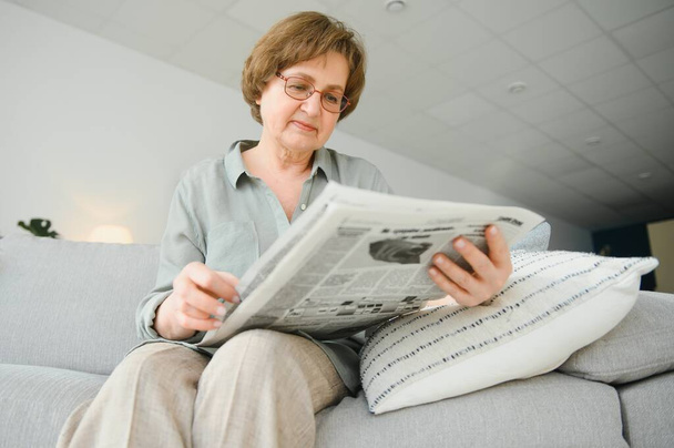 age and people concept - happy senior woman reading newspaper at home. - Фото, изображение