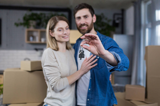 Selected focus, married couple man and woman happy together, hugging, holding the keys to their new apartment, housewarming, close-up photo - 写真・画像