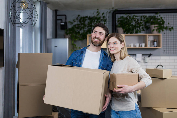 Happy couple man and woman live together, moved to a new rented apartment, holding cardboard boxes - Φωτογραφία, εικόνα