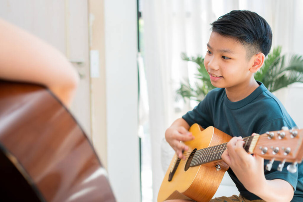 Ragazzo asiatico che suona la chitarra con il padre in salotto per insegnargli a suonare la chitarra, sentirsi apprezzato e incoraggiato. Concetto di una famiglia felice, apprendimento e stile di vita divertente, amore legami familiari - Foto, immagini