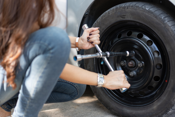 Smart and Attractive Asian woman jacks up her car and uses a wrench to change the wheel on a broken car, uses tools or equipment, tries to solve problems by self, Car Repairing and insurance concept - Photo, image