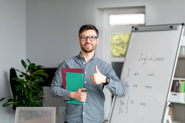 Pozitivní dospělý muž učitel ukazující palec nahoru stojící u tabule, doporučuje nové on-line cizích jazyků školy - Fotografie, Obrázek