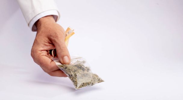 Pharmacy clerk hands over a bag of medical marijuana and takes the collection money with the other hand, on a white counter - Фото, изображение