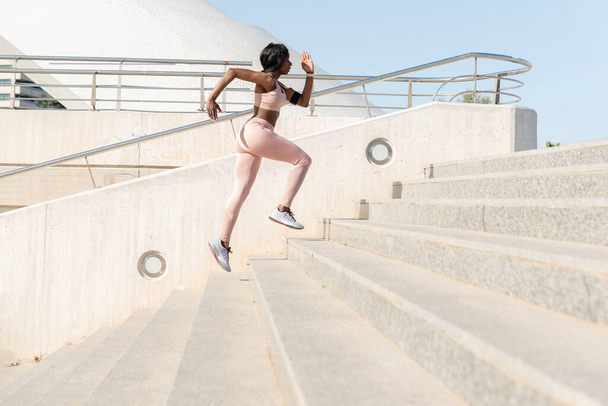 Vista lateral de una mujer africana corriendo escaleras arriba. Corredor mujer subir escaleras fitness, concepto de deporte - Foto, imagen