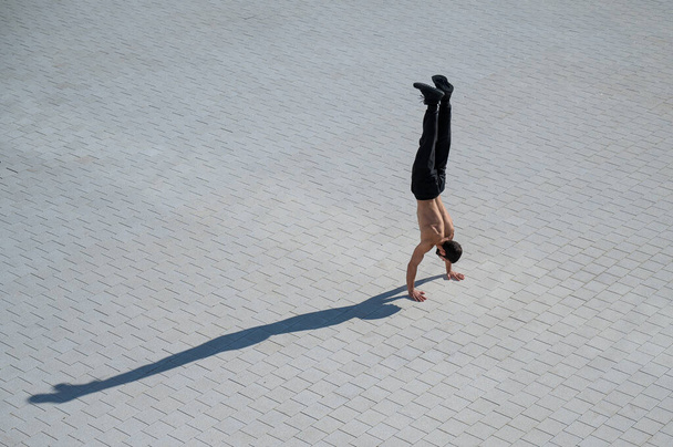 Shirtless man walks on his hands outdoors. View from above. - 写真・画像