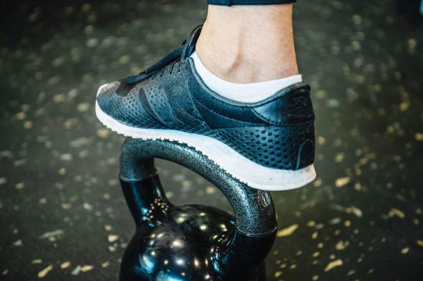 Stock photo of a detail of a footwear with sports shoes on a kettlebel in the gym - Photo, Image