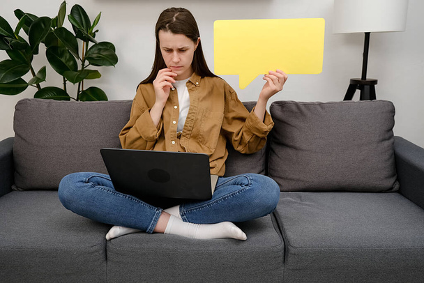 Young successful employee business woman sitting on grey sofa at home with pc laptop empty blank Say cloud yellow speech bubble promotional content prop up chin. Office workplace freelance concept - Foto, Imagem