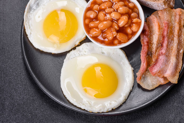 Desayuno inglés con huevos fritos, tocino, frijoles, tomates, especias y hierbas. Un comienzo abundante y nutritivo del día - Foto, Imagen