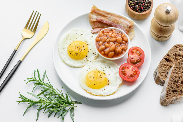 Anglická snídaně se smaženými vejci, slaninou, fazolemi, rajčaty, kořením a bylinkami. Srdečný a výživný začátek dne - Fotografie, Obrázek
