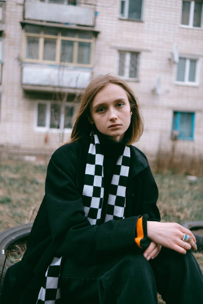 triest vluchteling meisje met blond haar zitten op de achtergrond van een oud gebouw in Oekraïne. - Foto, afbeelding