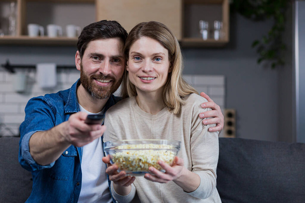 Photo of close couple man and woman together at home having fun and happily watching TV and eating popcorn - Foto, imagen