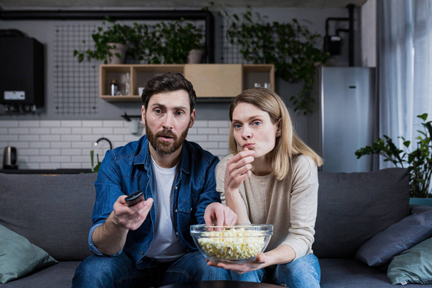 A man and a woman at home watching a boring movie, switching channels and eating popcorn - Фото, зображення